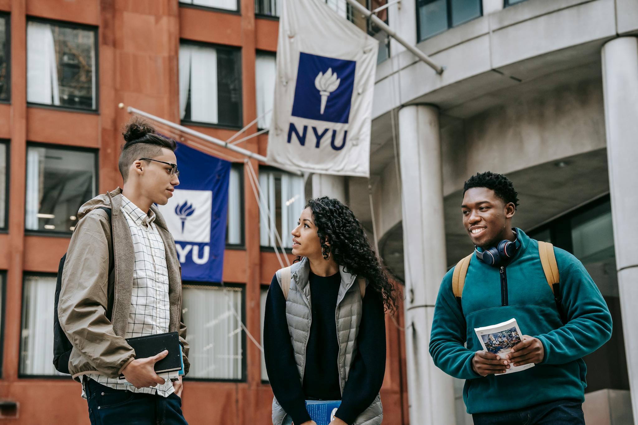 Group of diverse friends in casual clothes with papers standing near building and discussing details of university project