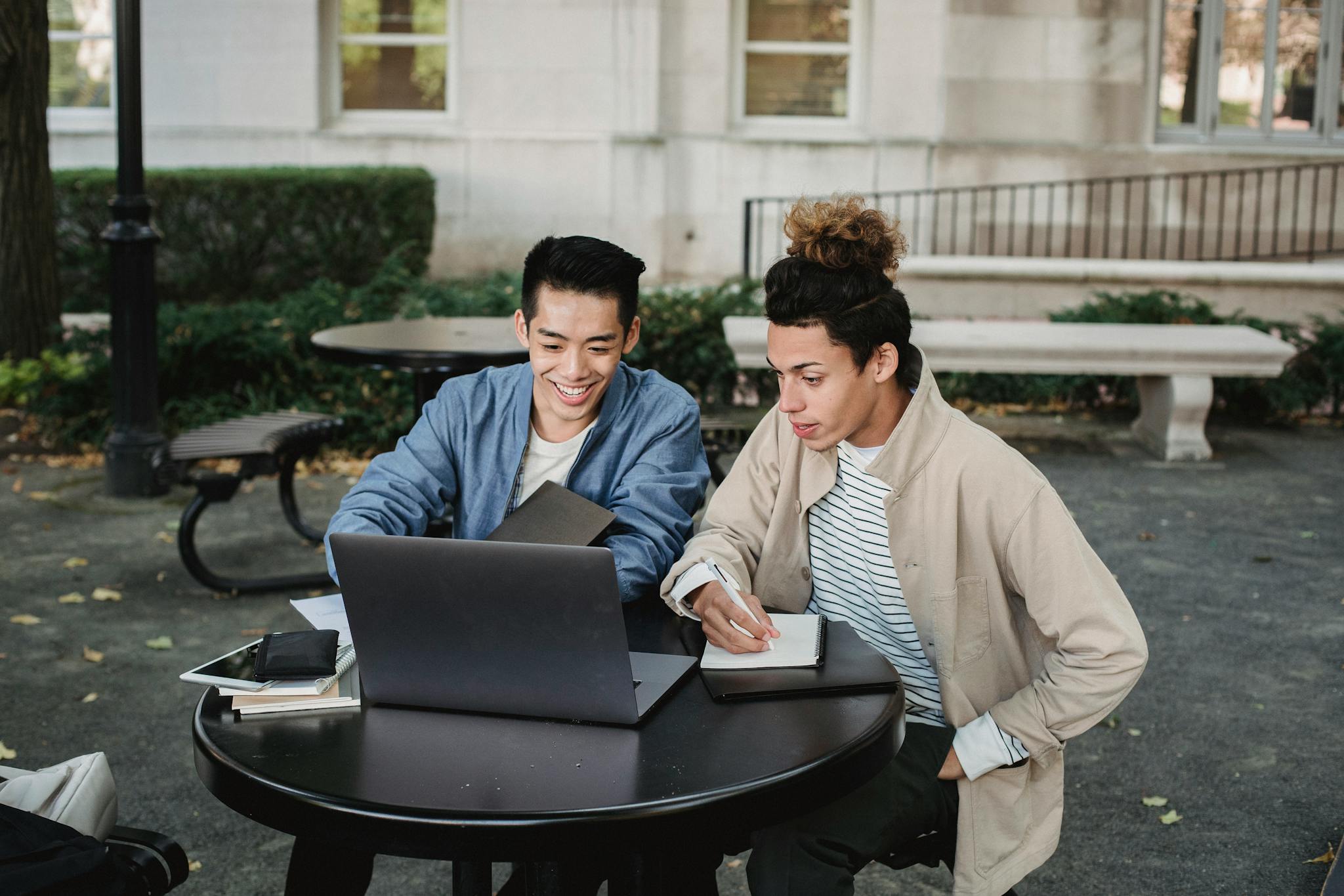 Two male university students collaborating on a laptop and notes outdoors.