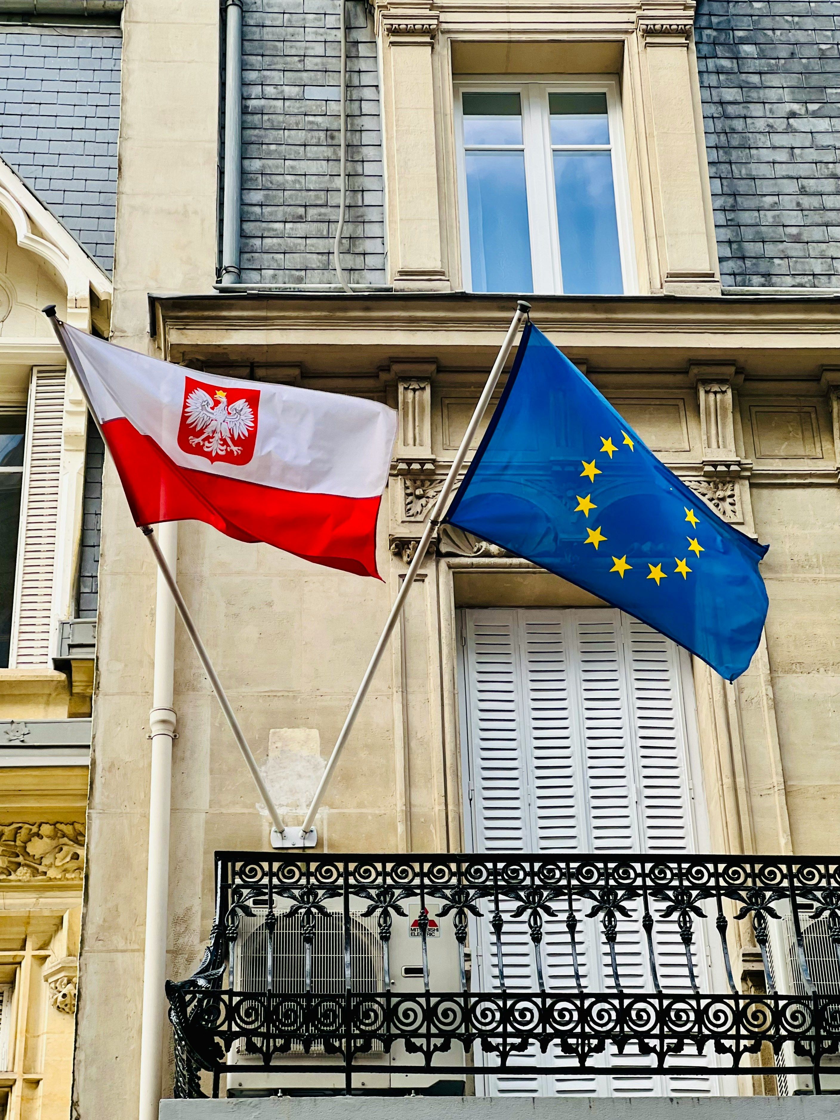 Two flags flying in front of a building in Poland