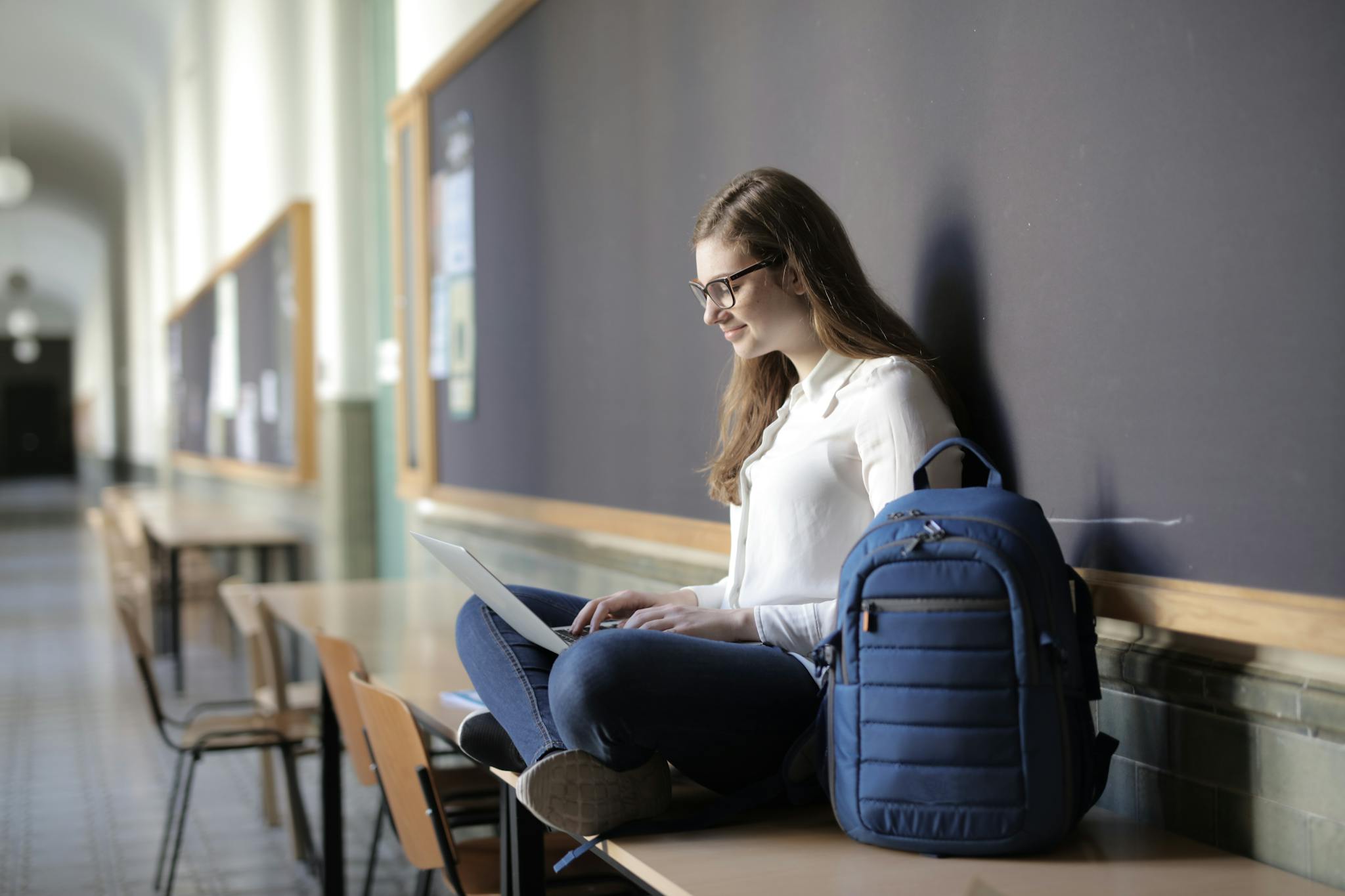 Smiling woman using a laptop in a school hallway, representing remote learning.